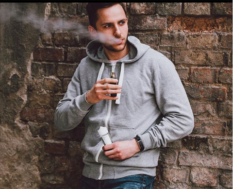 man standing in front of brick wall vaping
