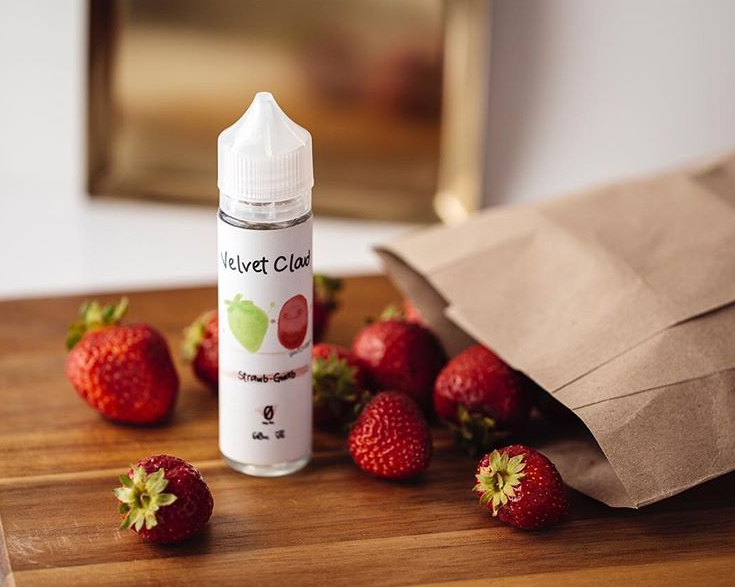 a bottle of Velvet Cloud fruit-flavored e-liquid on a table with strawberries