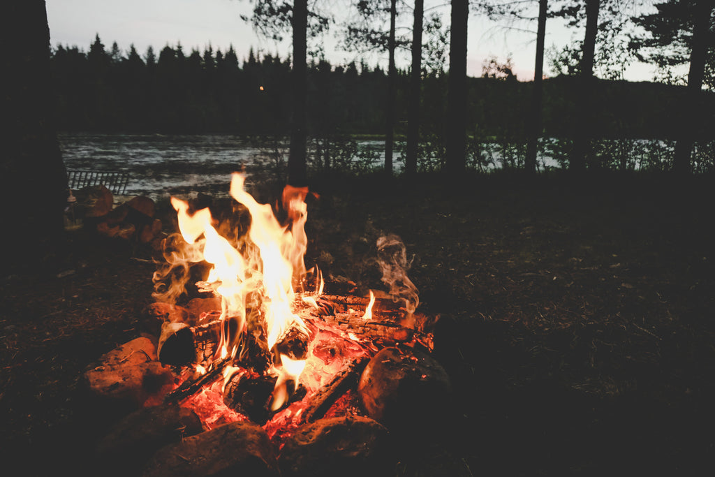 picture of a campfire near a river at sunset