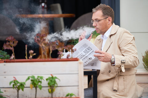 businessman sitting at cafe vaping and reading newspaper