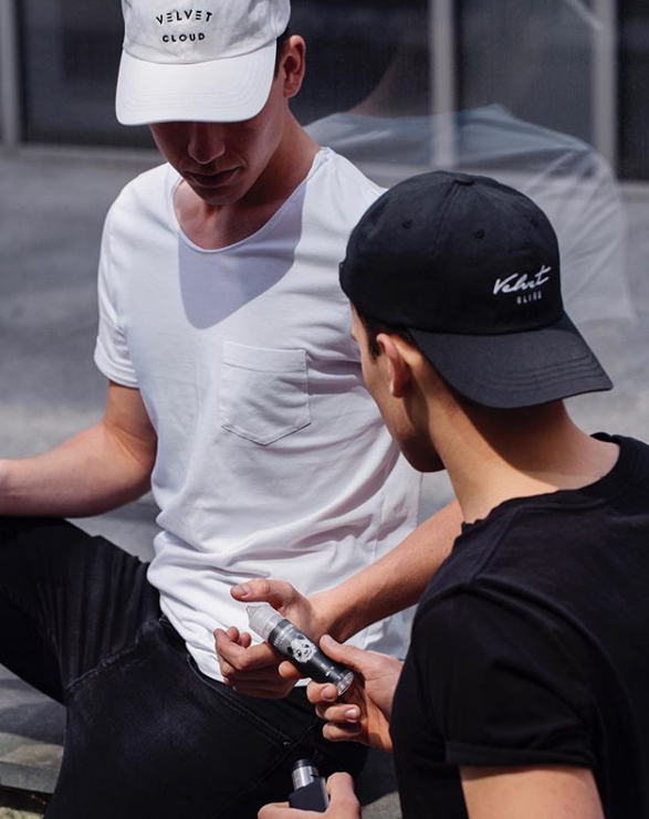 two men in Velvet Cloud hats; one is handing a bottle of e-liquid to the other