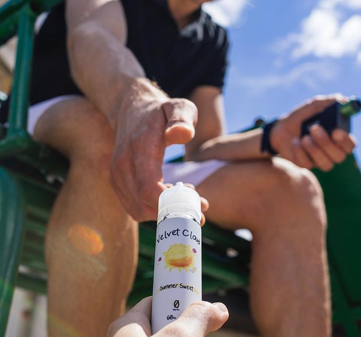 a hand giving fruit-flavored e-liquid from Velvet Cloud to a man sitting on a bench