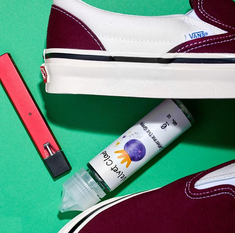 bottle of grape-flavored e-juice between a pair of red and white shoes