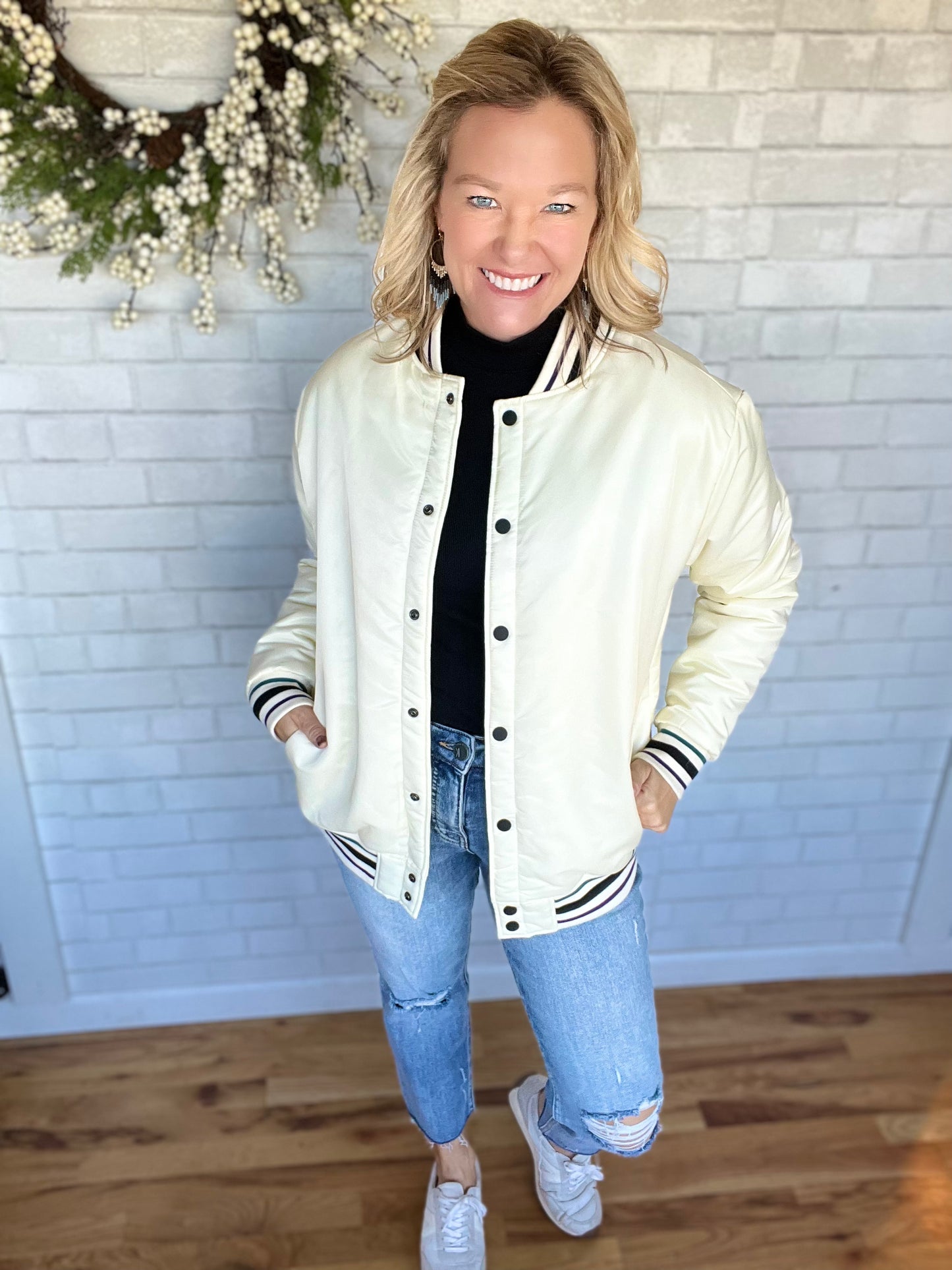 A white letterman jacket with black and green striping on the sleeves and the the hem. Pockets on the side and buttons for closure on the front. Fit is true to size.
