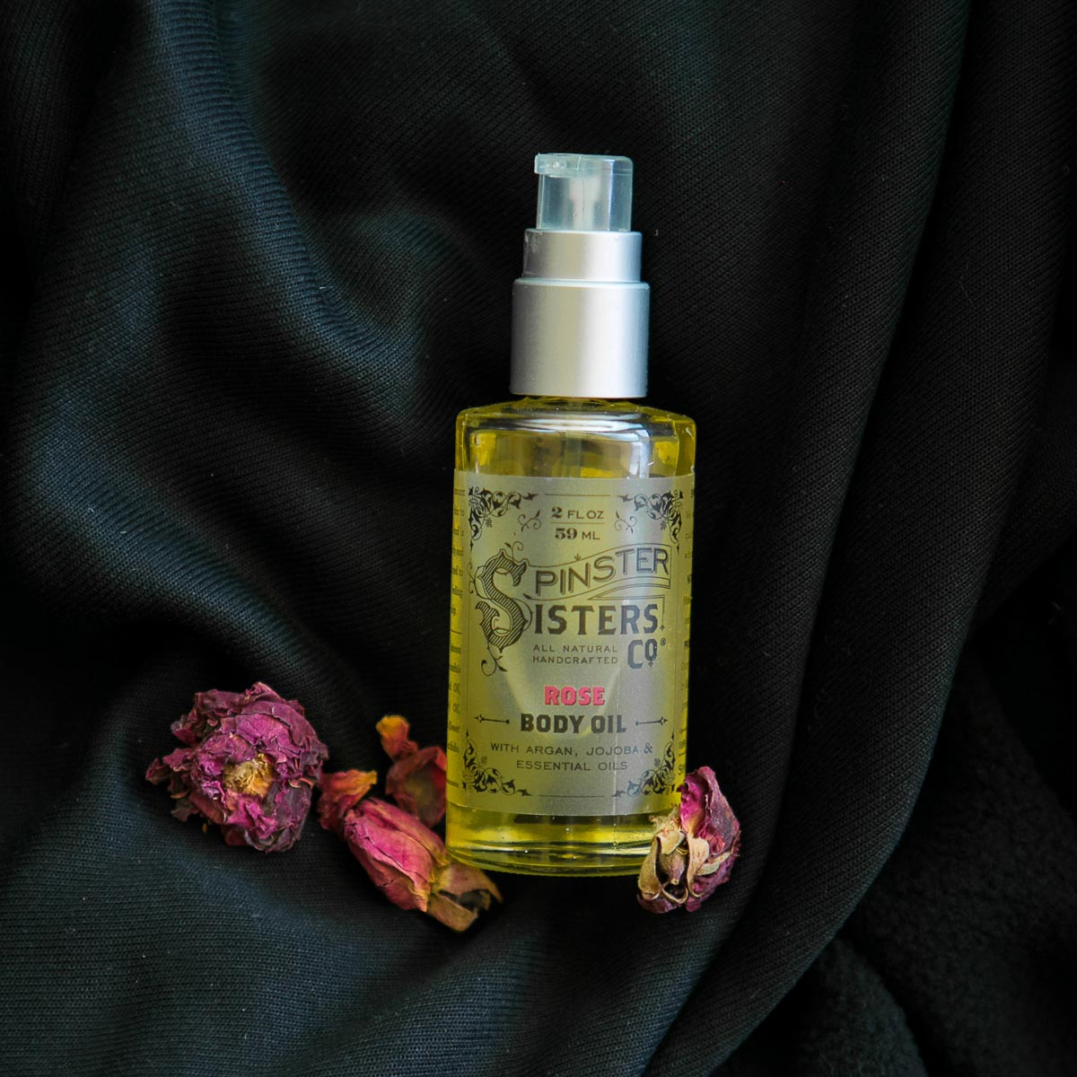 A clear bottle of yellow-hued Body Oil styled with dried rose petals
