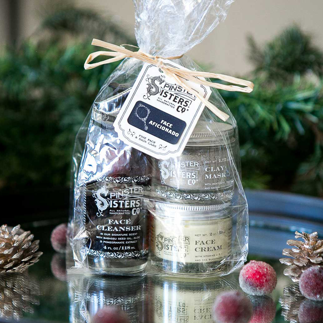 A clear bag with a raffia bow holds face moisturizer, clay mask, and face cleanser