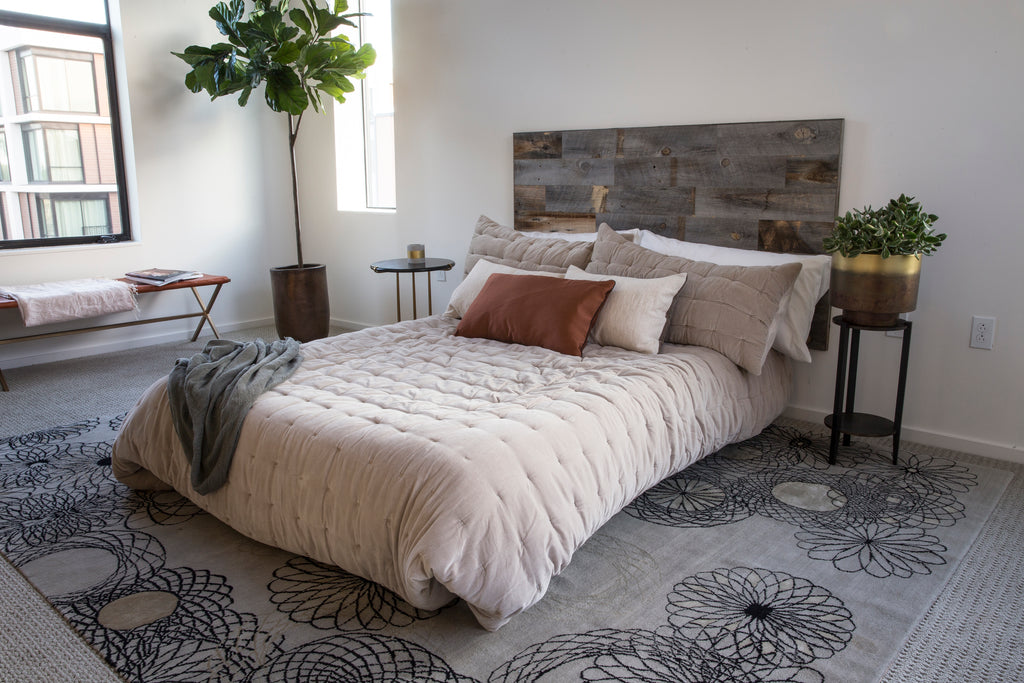 Queen size DIY reclaimed headboard is attached to a white wall and has pillows piled against it.