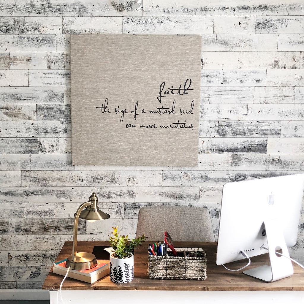 An organized desk with a faith sign that is hanging on a modern wood wall.