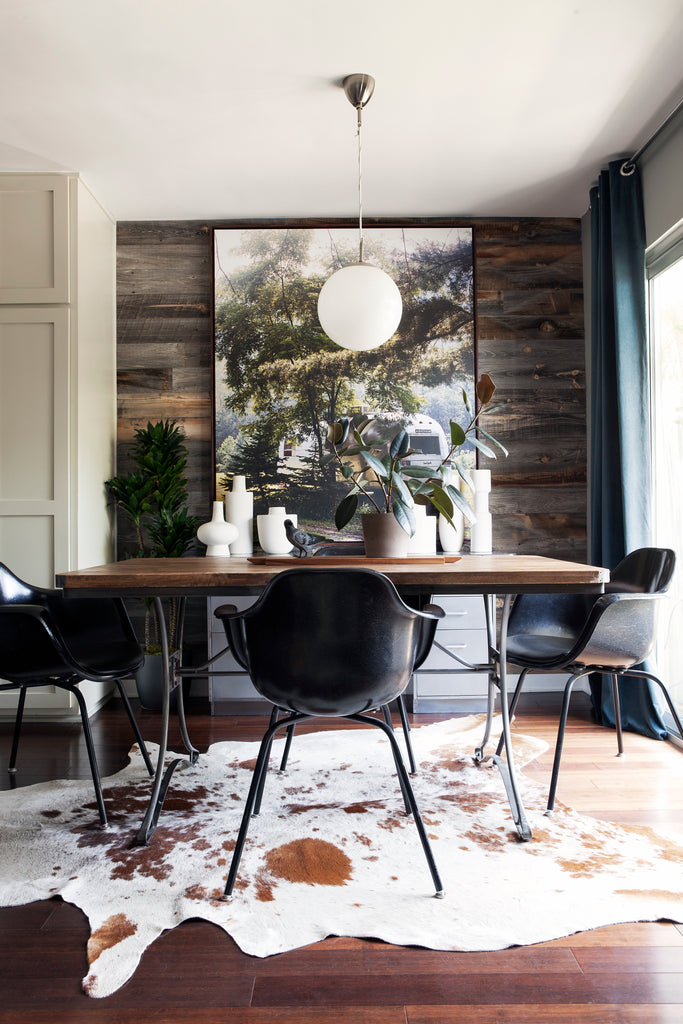 Barn wood wall paneling and a cow hide rug add rural feel to a dining room. 