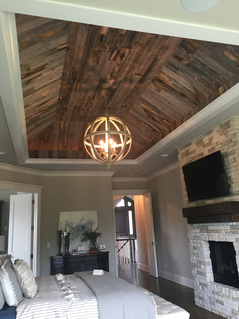 Ceiling wood planks are applied to a tray ceiling and paired with a white orb light in a contemporary master bedroom.