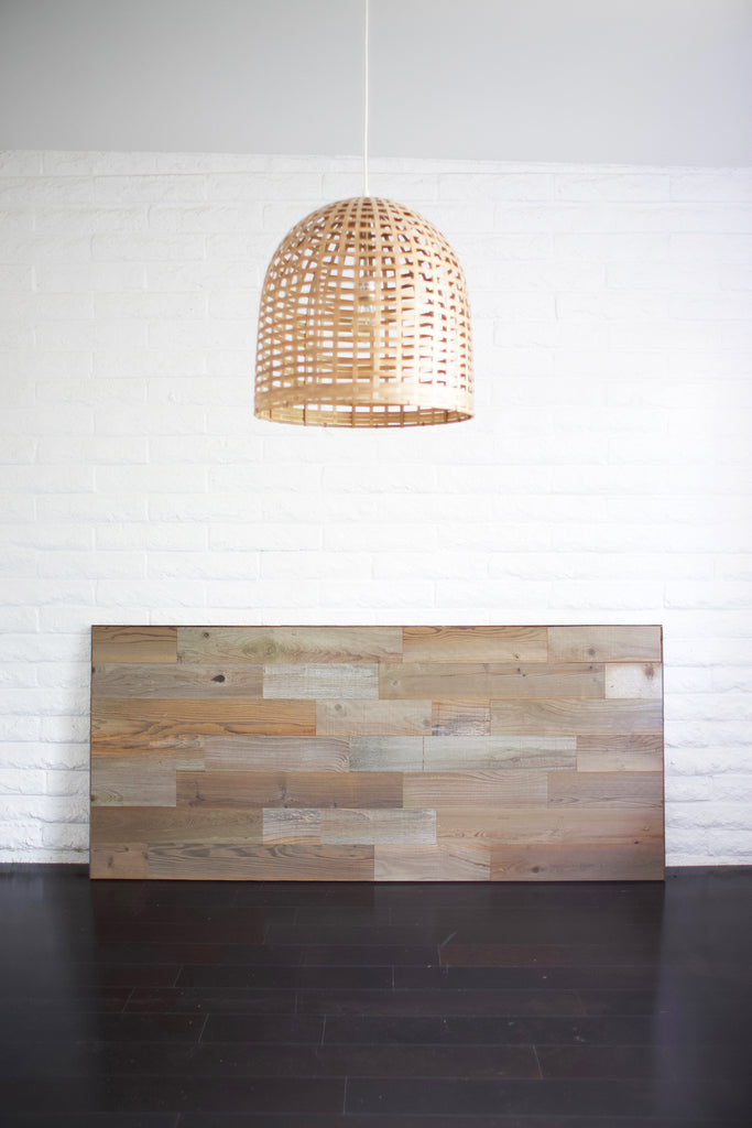 A finished reclaimed wood headboard diy project is leaning against a white brick wall.