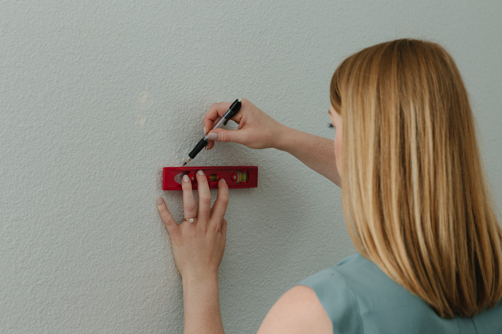 A woman using a level and a pencil to draw straight lines onto a wall prior to timberwall peel and stick installation.