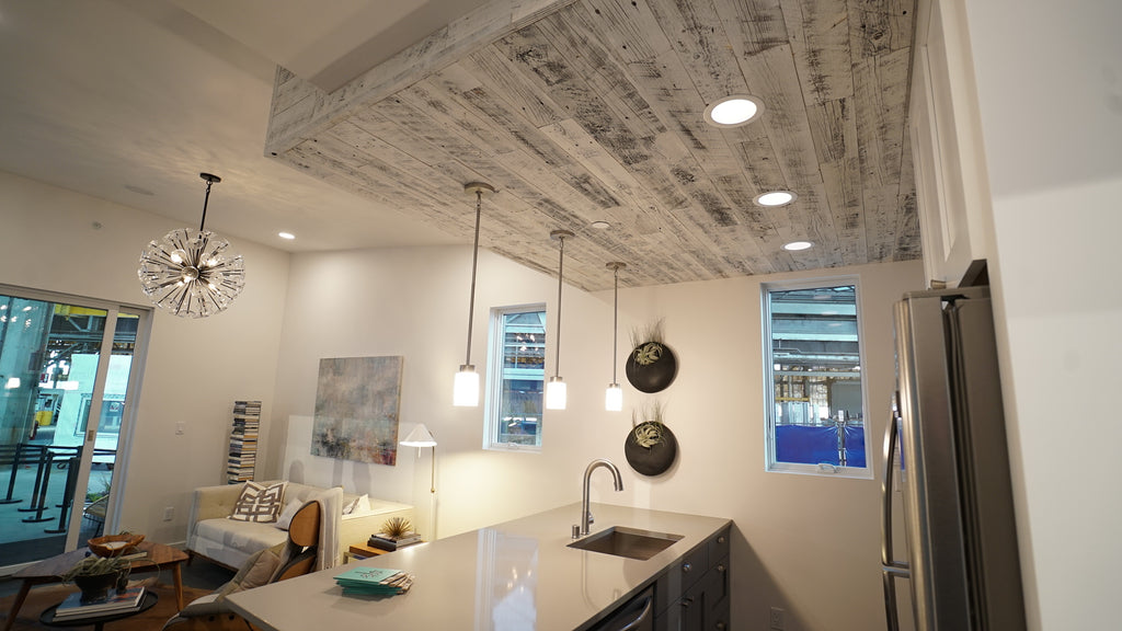 Reclaimed Weathered Wood White reclaimed wood paneling helps differentiate a kitchen space in an open floor plan by being added to the ceiling. 