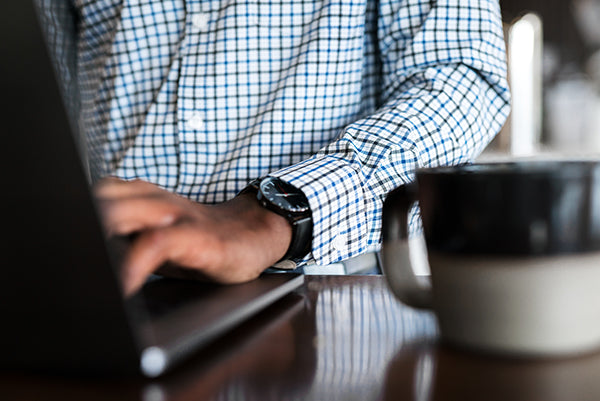 Working at a laptop computer with a cup of coffee while wearing the Meridian performance dress shirt.