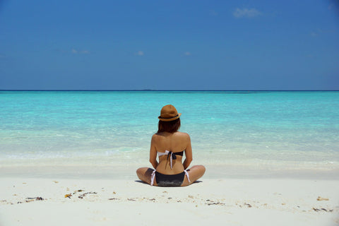 ragazza seduta fa yoga in spiaggia con sabbia chiara e acqua caraibi