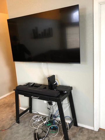 Living room with wall mounted TV, table with devices and messy cable clutter on floor