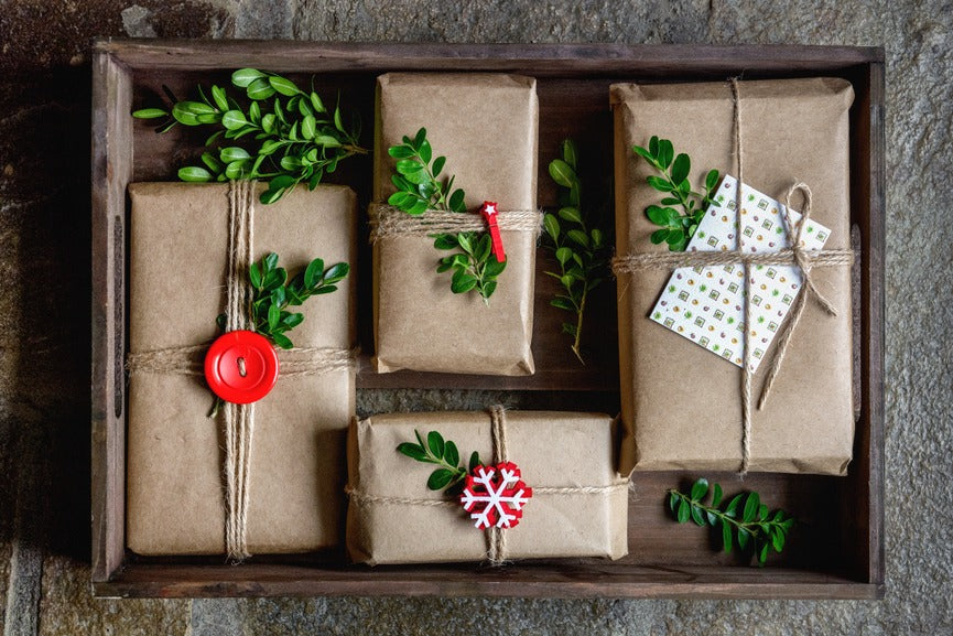 wooden crate filled with four presents wrapped in packing paper and decorated with leaves