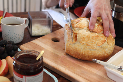 Cutting a loaf of crusty bread next to jar of strawberry limoncello deliciousness jam  