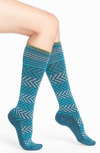 A pair of legs wearing Sockwell socks that are teal and white with a chevron pattern.