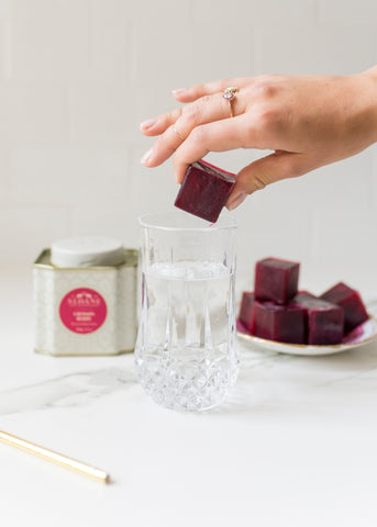 hand placing crimson berry iced tea ice cube in glass