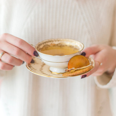 person holding tea cup with crisp on plate
