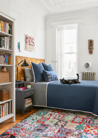 Apartment interior bedroom with indigo bedspread and Coral and Tusk pillows, black cat relaxing on the bed.
