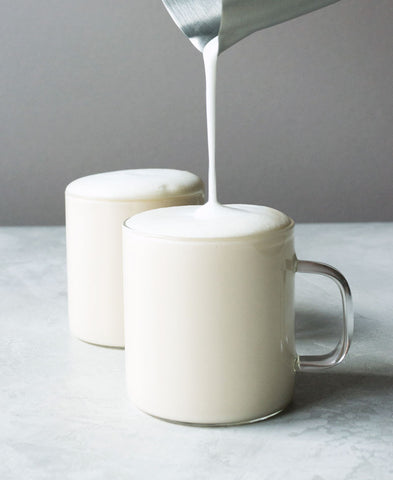 a silver pitcher pours frothed milk into two mugs of vanilla tea