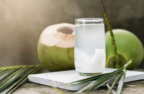 coconut water in glass on marble counter with coconuts in back