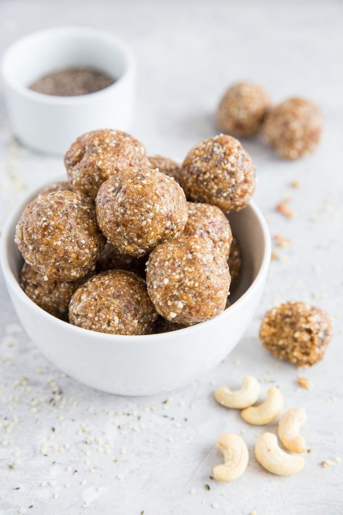 Homemade fig and date cashew energy balls sit in a white bowl with cashew halves sprinkled nearby.