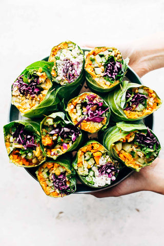 hands holding out a platter with a selection of halved rainbow rolls full of colorful vegetables