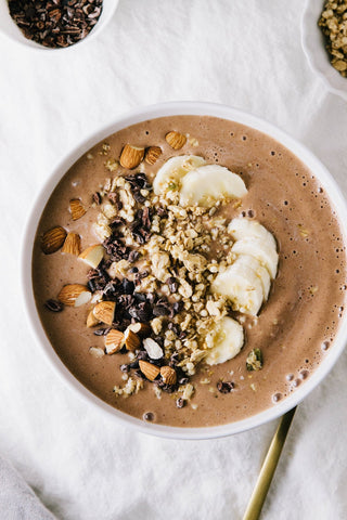 a chocolate smoothie bowl topped with chopped nuts cacao nibs and bananas