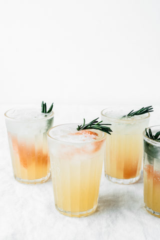 four glasses filled with rosemary honey grapefruit spritzer garnished with rosemary