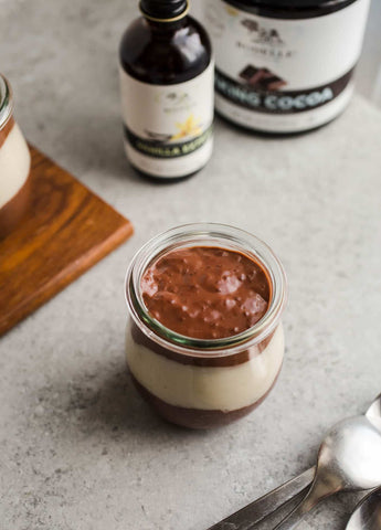 vegan chocolate pudding cups layered next to wooden board and jars of vanilla and cacao powder