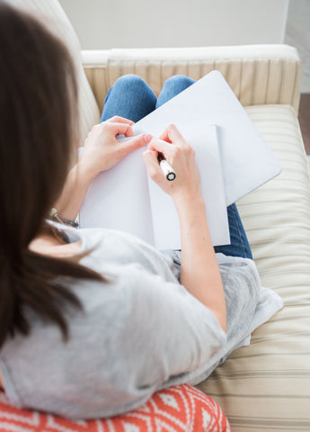 Woman sitting on couch, writing in a journal
