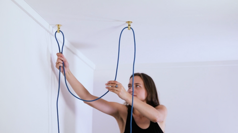 Woman hanging blue light cord on ceiling hooks