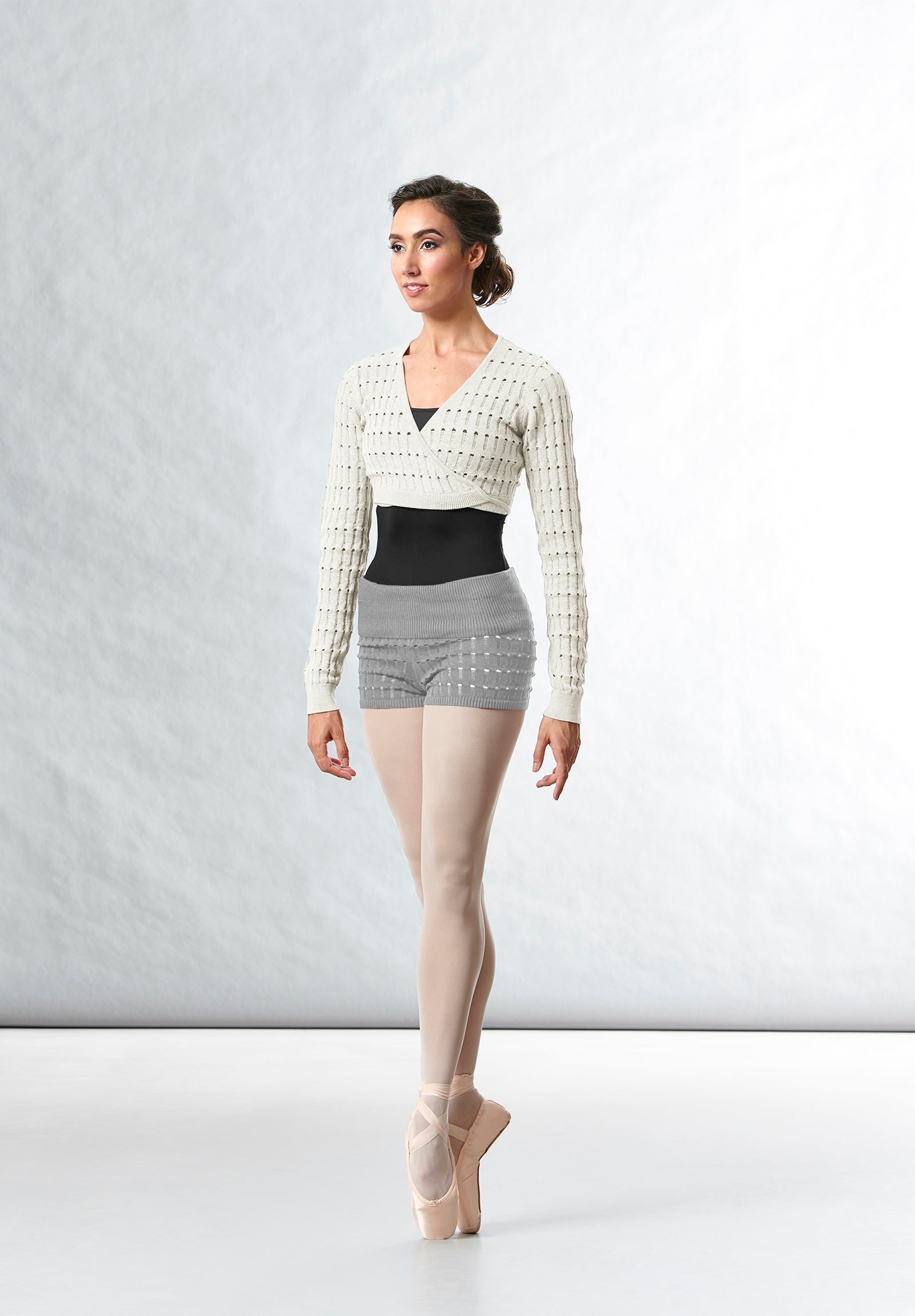 A female ballet dancer wearing a black BLOCH leotard, knitted wrap top and shorts