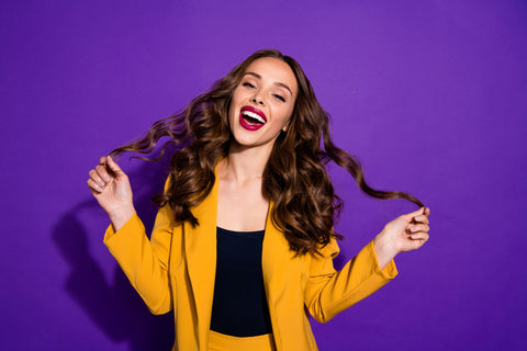 brunette woman smiling and holding curly hair on purple background