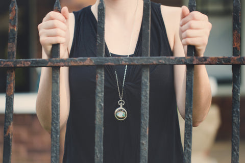 White woman behind bars with celestial pocket watch necklace
