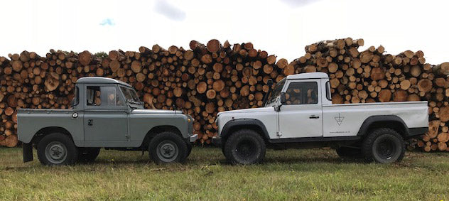 Landrovers in front of log pile
