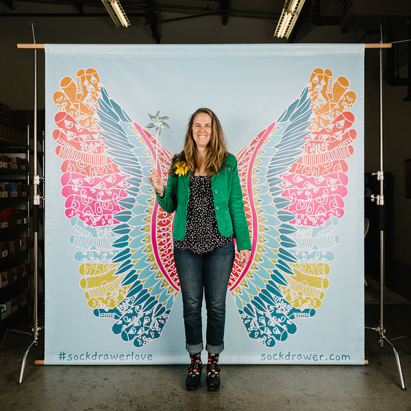 Brooke English posing in front of a mural with sock fairy wings