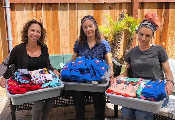 The Sock Drawer employees holding bins of socks for donation to Rita's Rainbows