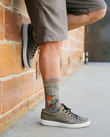 A man wearing funny socks that say, "Here comes cool dad"