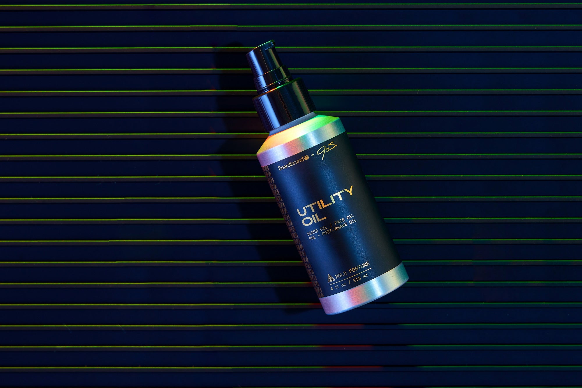 A bottle of special-edition Beardbrand Bold Fortune Utility Oil highlighted with a rainbow sheen on dark neon-striped background.