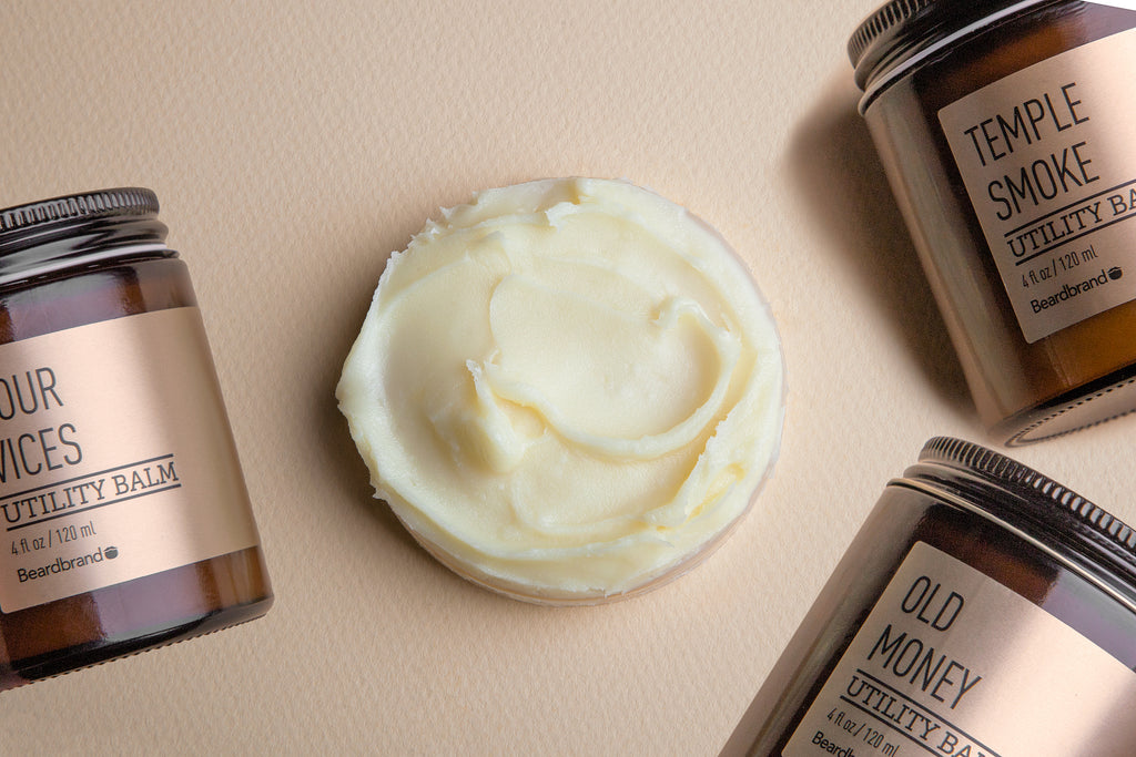 A circular scoop of Beardbrand Utility Balm on a table, surrounded by three jars of Beardbrand Utility Balm