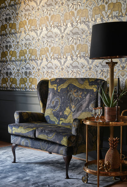 A chair upholstered in the luxurious Lynx Grey Velvet fabric perfectly matched with the Zambezi metallic gold wallpaper, designed by Emma J Shipley in collaboration with Clarke & Clarke
