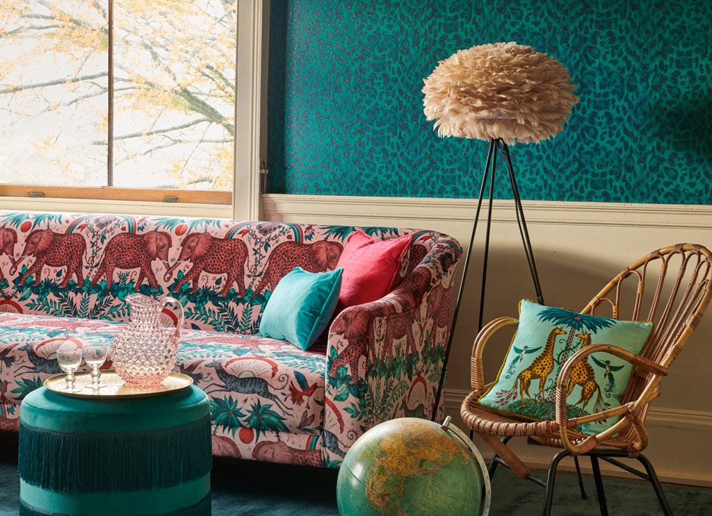 A sofa upholstered in the Zambezi Pink Velvet fabric, paired with a turquoise Creatura Cotton Satin cushion and the Felis Wallpaper in Teal. Creating the perfect maximalist home interior