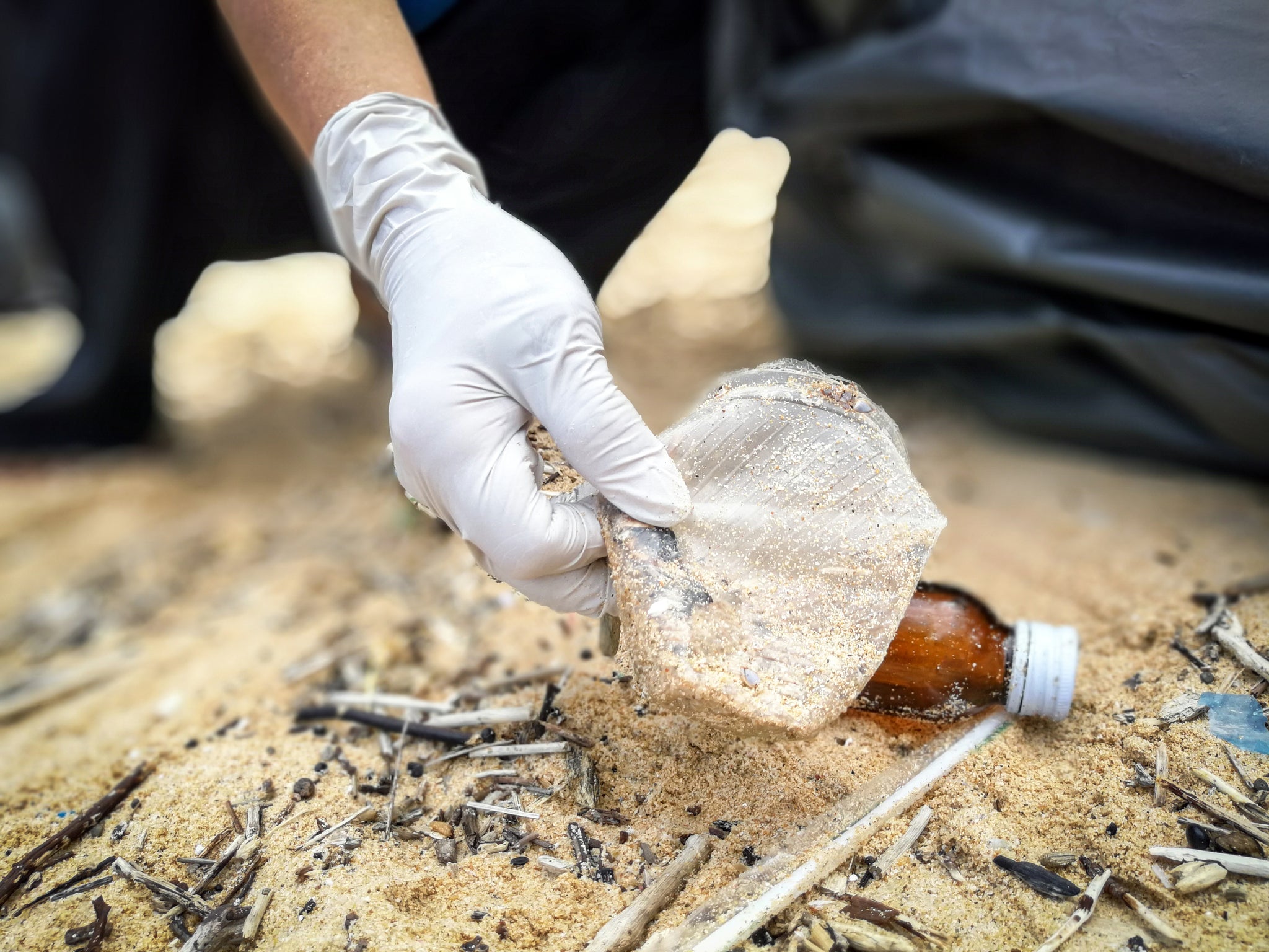 gloved hand picking up plastic trash on the beach