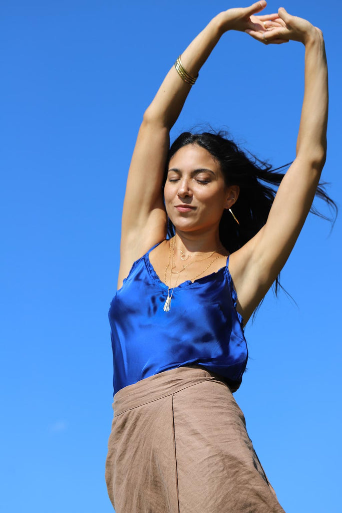 girl stretching in front of blue sky with layered delicate gold jewelry