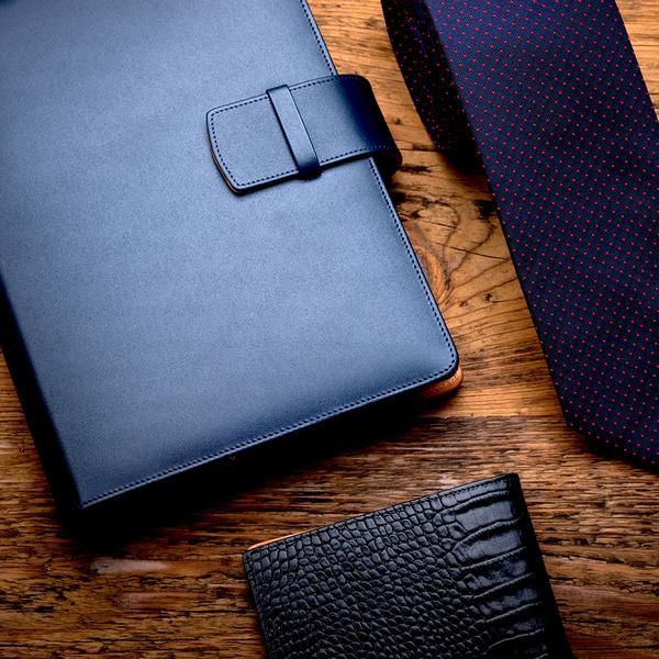 Kožený diář, pánská kravata a pánská kožená peněženka ležící na stole