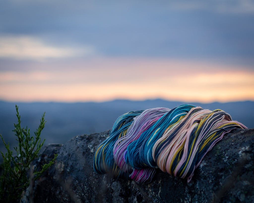 yarn sits on a rock in front of a sunset gauge dye works self striping